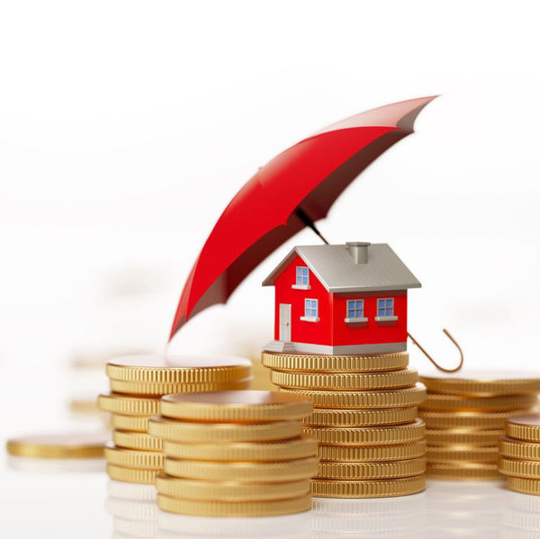 Model house, shielded by umbrella, sitting on stack of gold coins