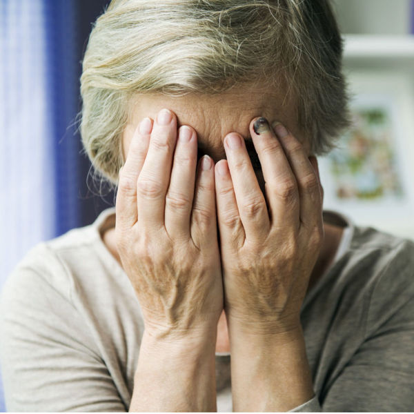 Photo of an elderly woman covering her face with her hands