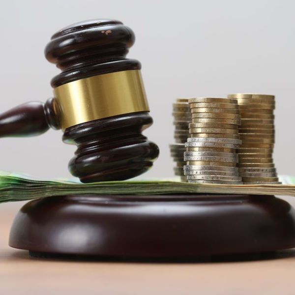 gavel resting on thin stack of currency next to stacks of coins