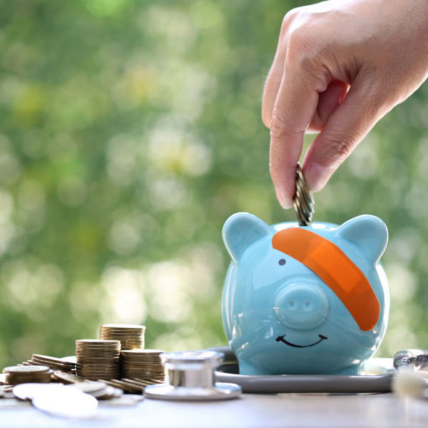 Piggy bank wearing a Band Aid over one eye while someone deposits coins in it