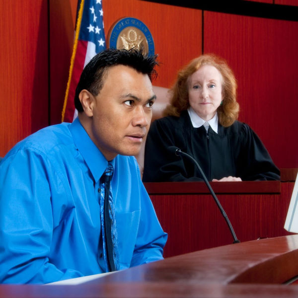 Gentleman giving court testimony while judge looks on from background