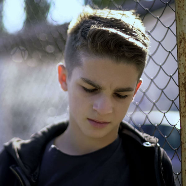 Teen male looking sad in front of a chain link fence