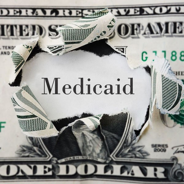 dollar bill with center torn out, revealing the word Medicaid behind it